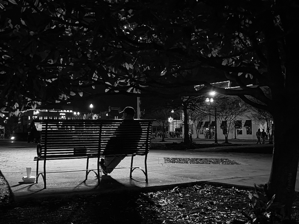 Photograph of an older man sitting alone on a park bench.