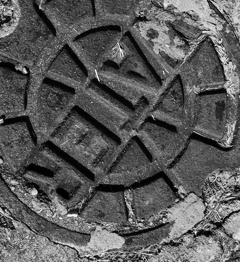 A black and white photographed image of the top of a sewage water drain.