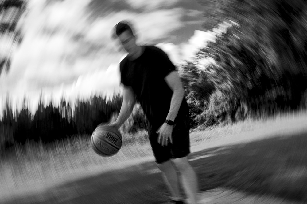 A black and white photographed image of a man dribbling a basketball.