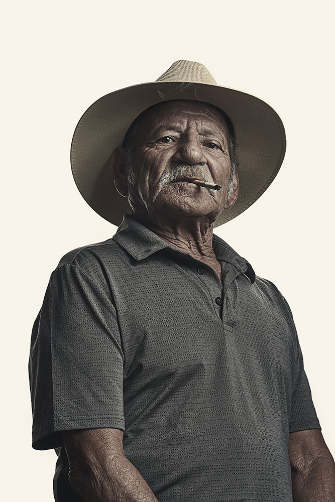 Photo by Kamau Bostic shows an older man with a cigarette in his mouth looking down at camera - wears a cowboy style hat