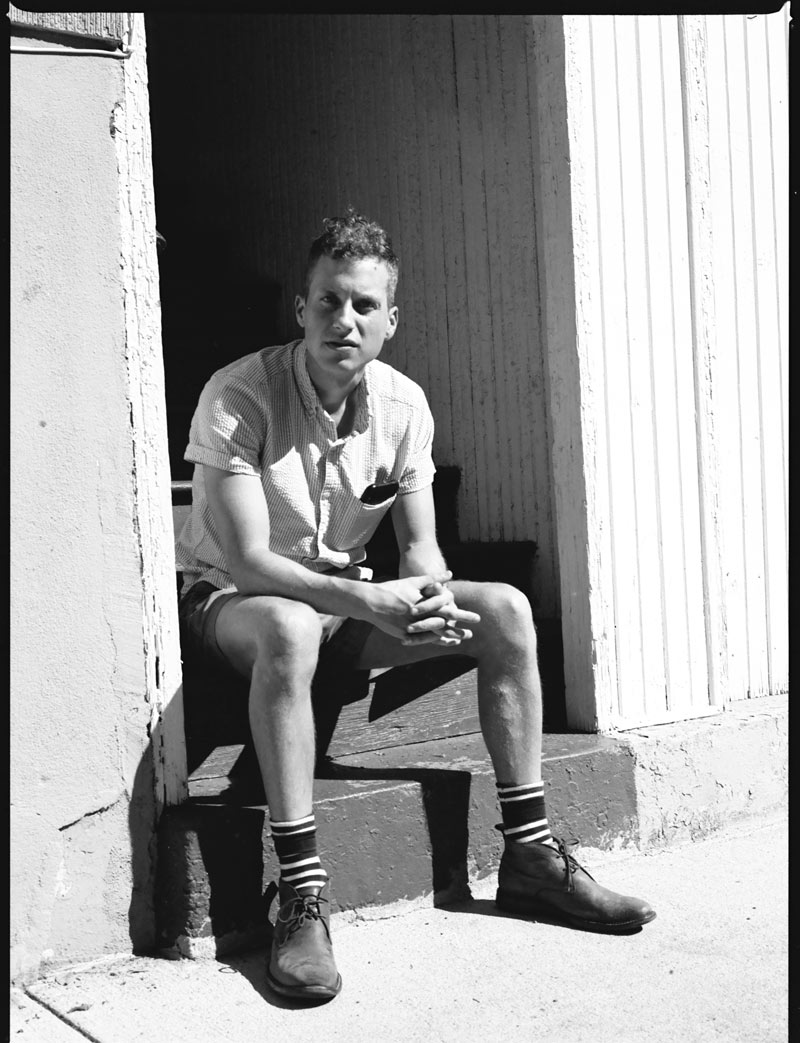 Whitten Sabbatini sitting on steps outside leaning forward with his hands clasped, staring at the camera.