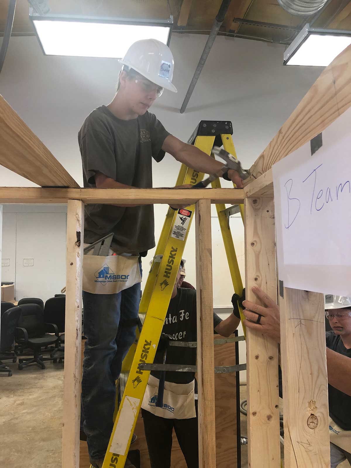 student on ladder hammers frame together for shooting house