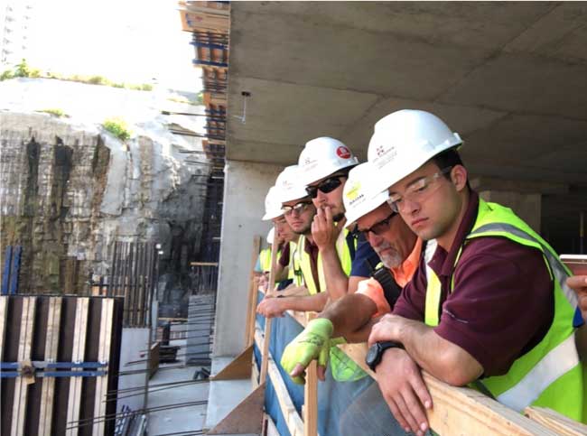 Building Construction Science students wearing hard hats lean on rail 