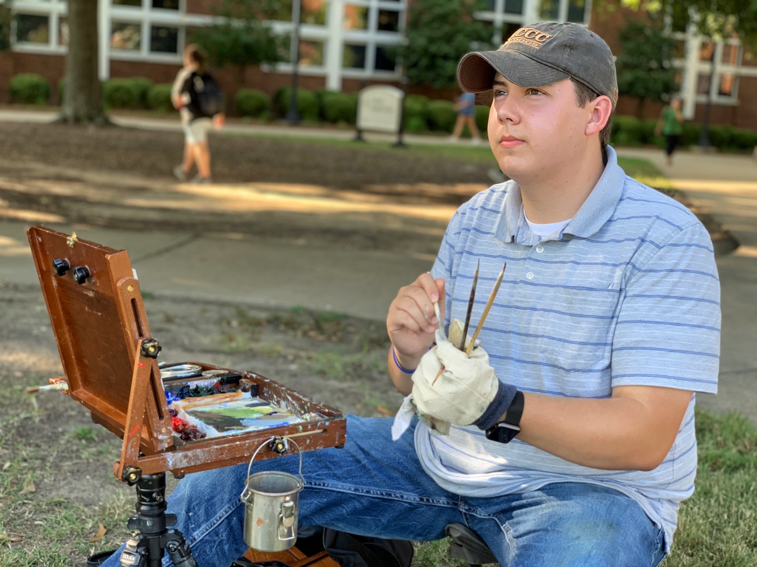 Fine arts major Garrett Seal sits with paint equipment on campus drill field