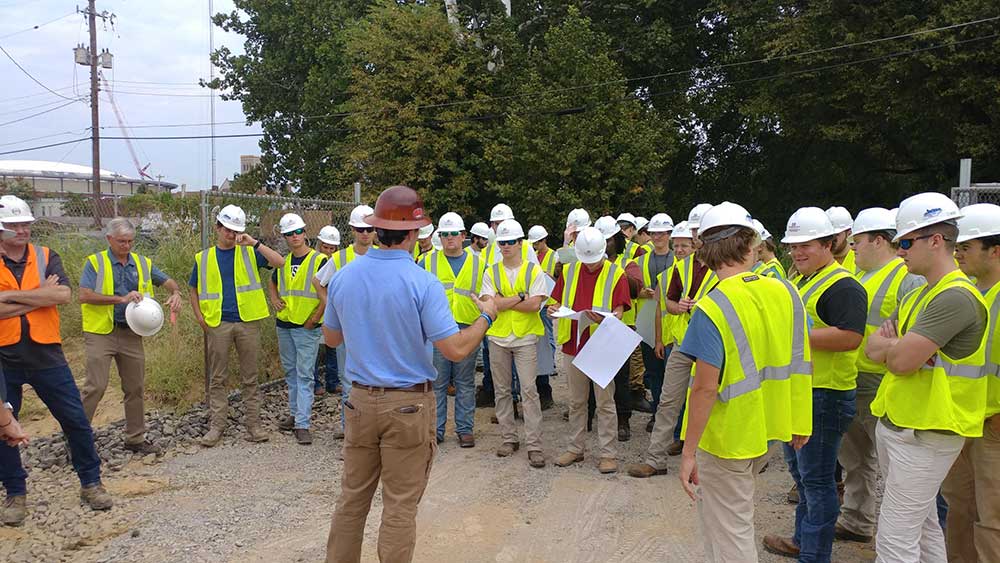 Mississippi State building construction science freshmen listen on job site - wearing safety vests and hard hats