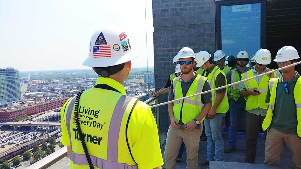 Building Construction Science students wearing safety vests and hard hats listen on a field trip with a view of Nashville