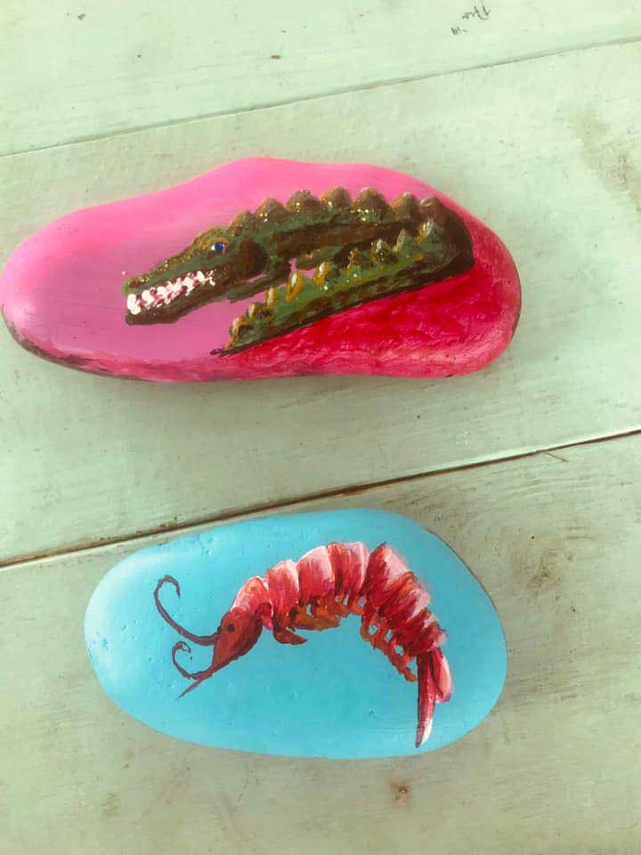 two painted rocks - one is pink with an alligator and the bottom one is light blue with a shrimp or lobster