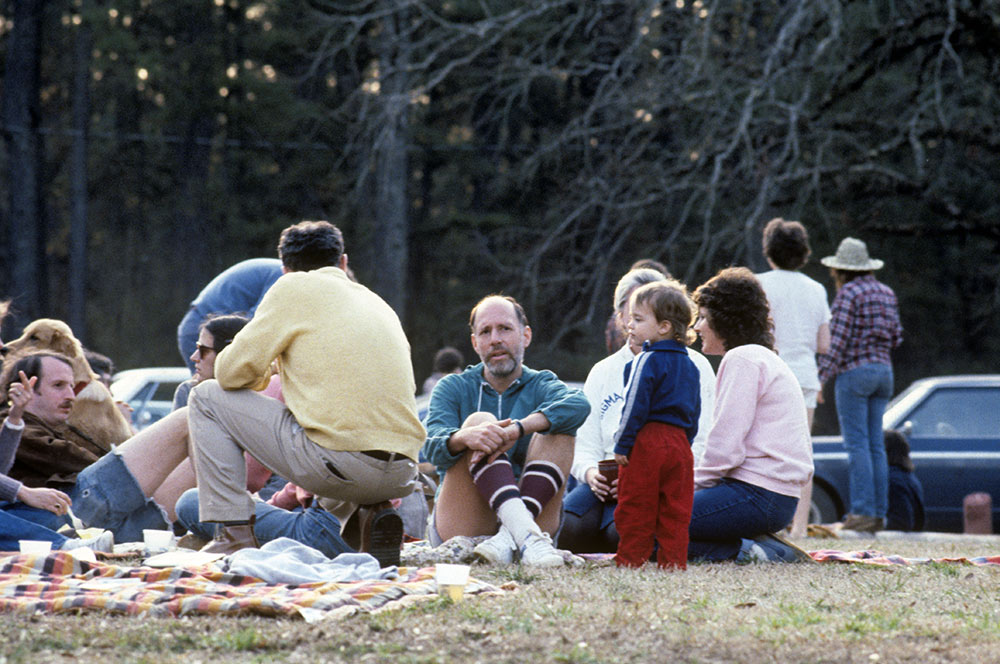 Michael Fazio, facing front, center, sits with a group on the grass. Looks like a picnic