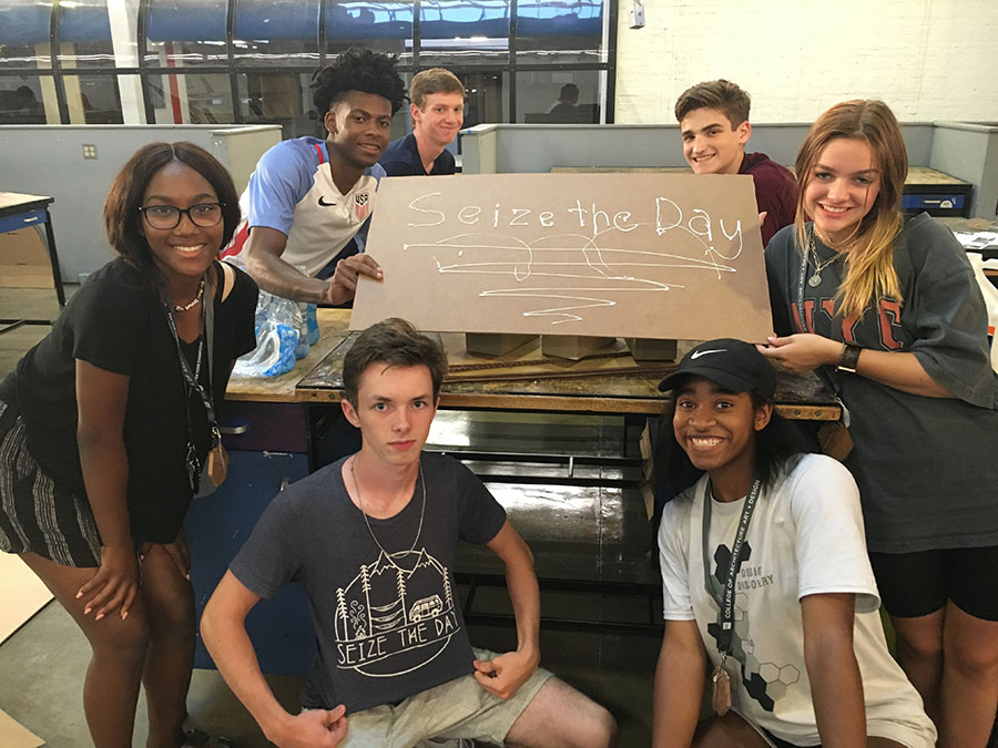 a group of campers holds a hand-made cardboard sign that reads, &quot;seize the day&quot; in white paint lettering
