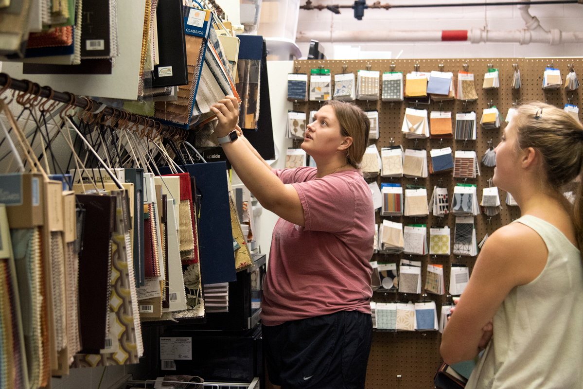 Two Students look through rows of fabric inside of the interior design storage room