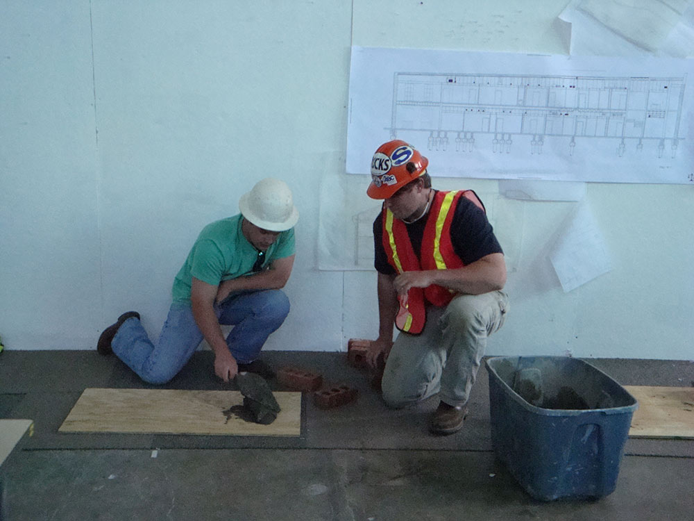 2 people in construction ppe kneel over concrete on board