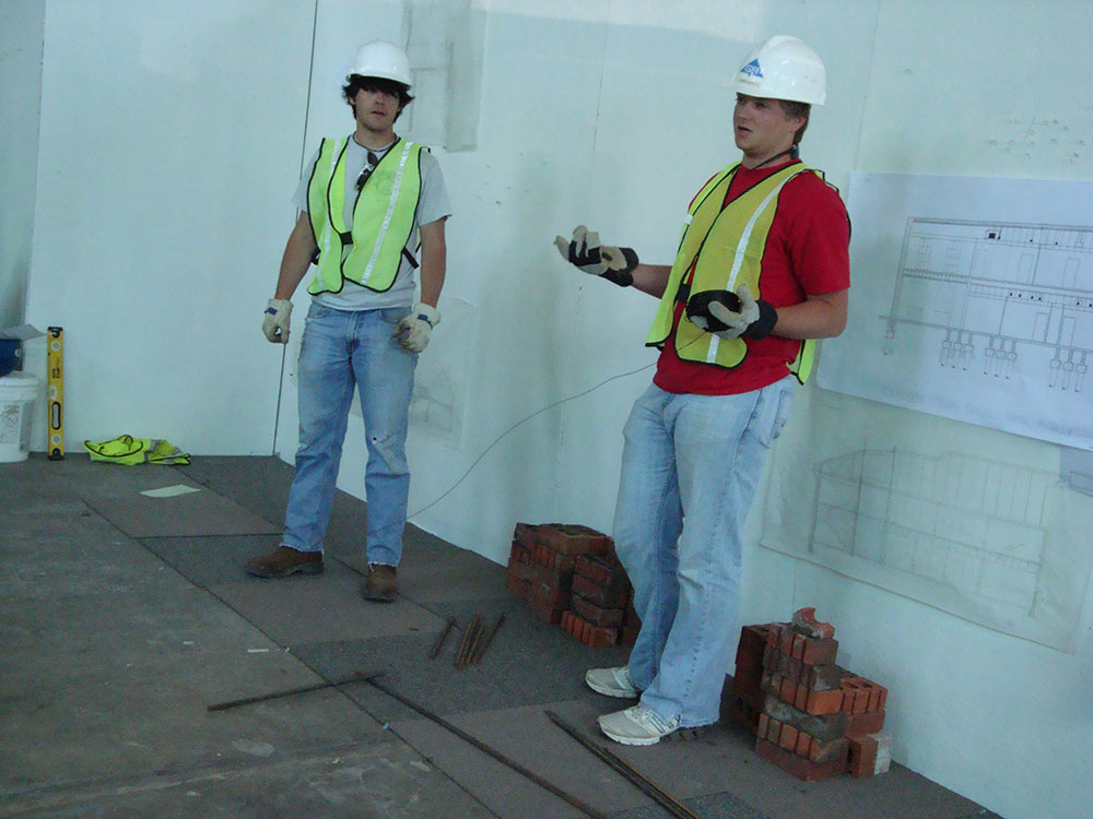 2 people wearing construction hats look to be explaining something