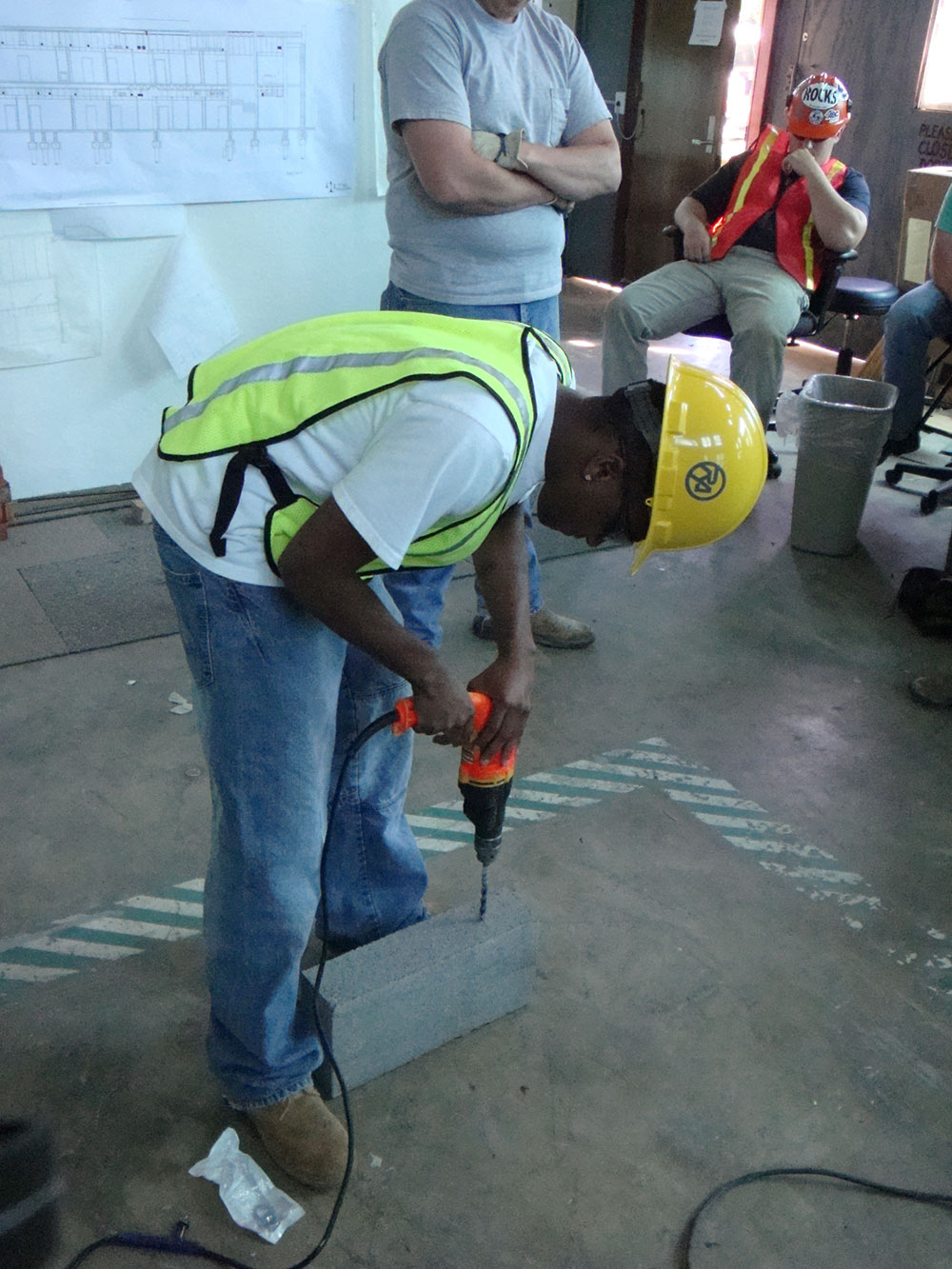 person wearing construction hat, drilling into concrete block