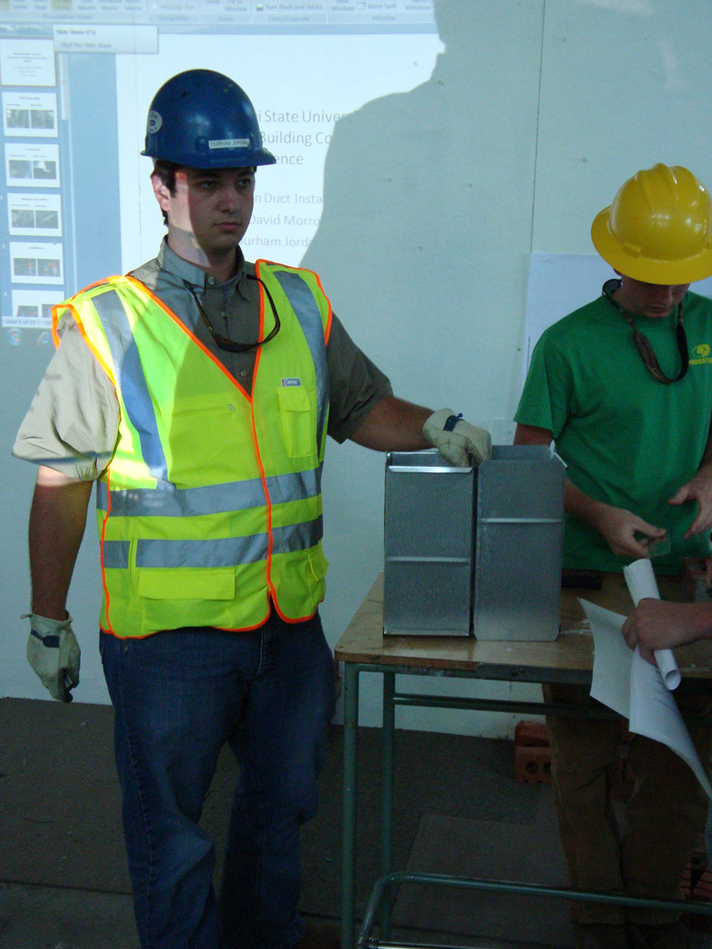 person wearing construction PPE rests hand on metal piece