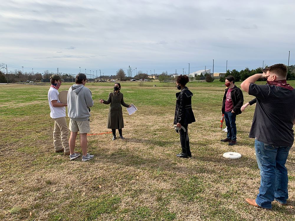 students stand in grass listening to Professor Silvina Lopez Barrera