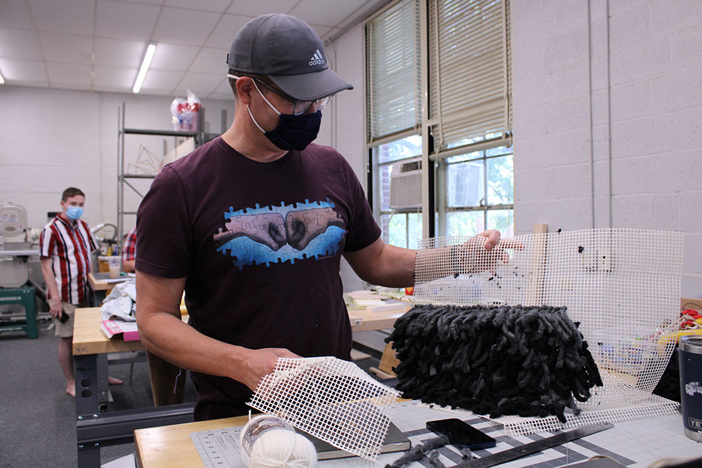 male student works on what looks like long black shag rug project
