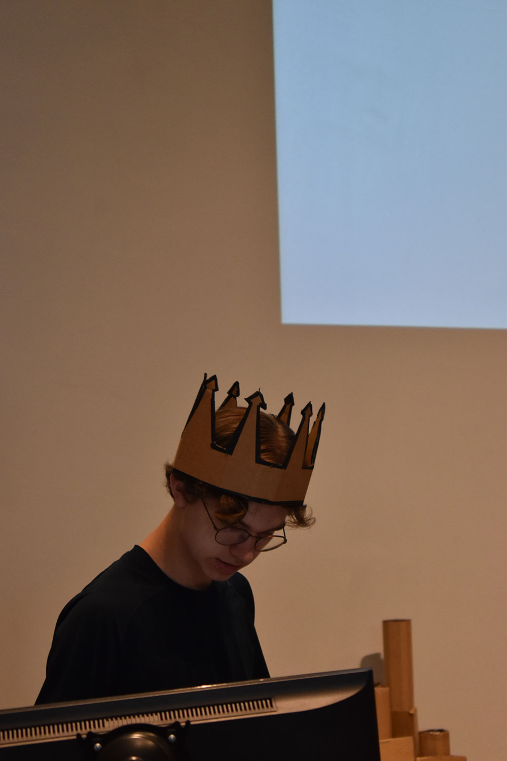 camper wearing crown made of cardboard stands behind lecturn