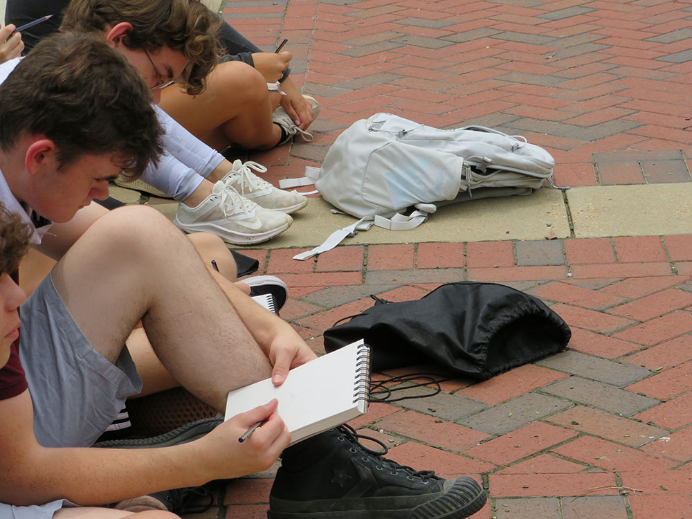 campers sit on sidewalk and sketch