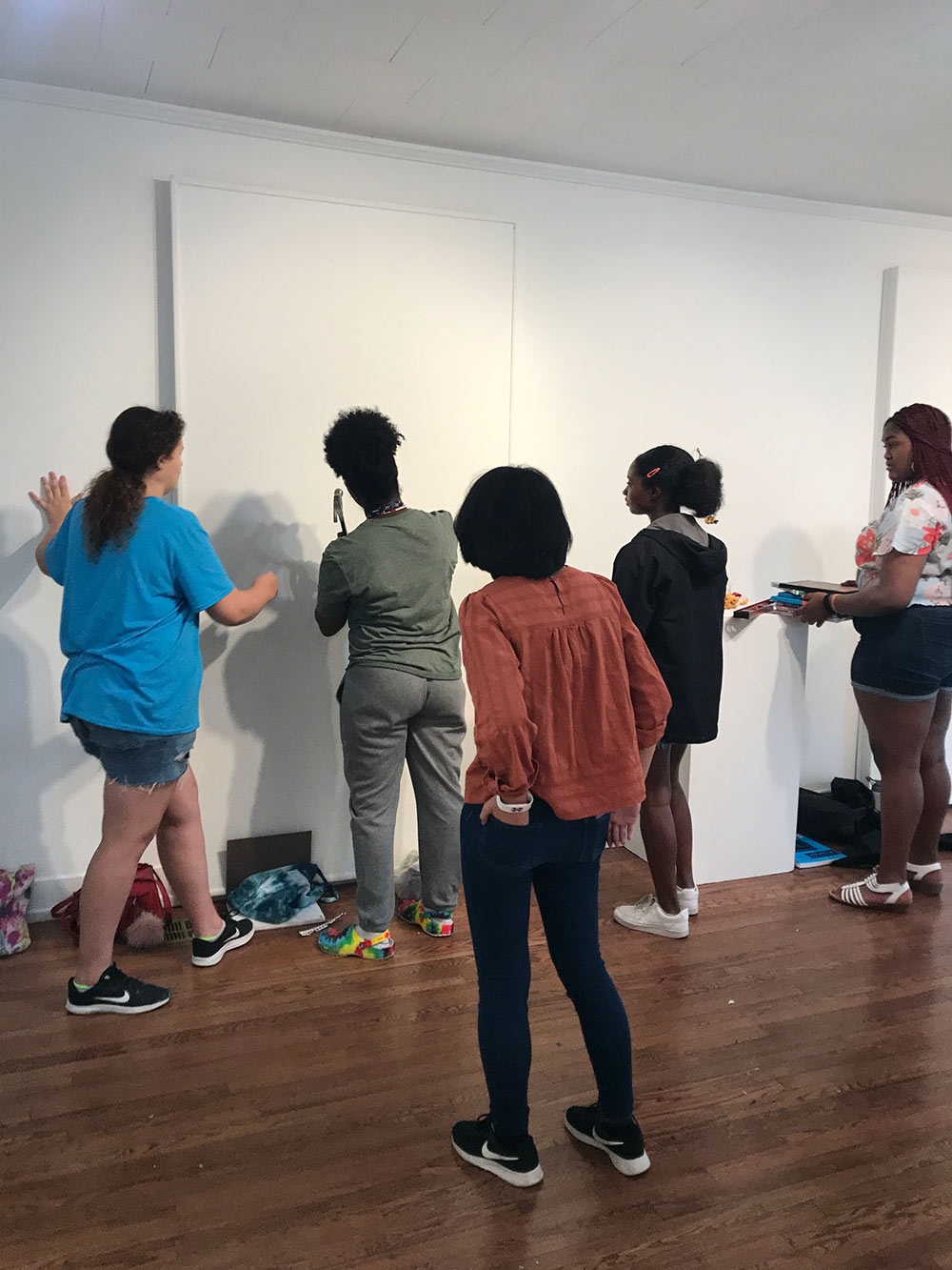 counselor hammers work on wall in Visual Arts Center Gallery as campers look on