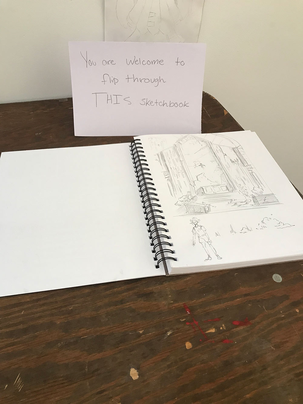 sketchbook open to page with sign behind that says &quot;You are welcome to flip through THIS sketchbook&quot;