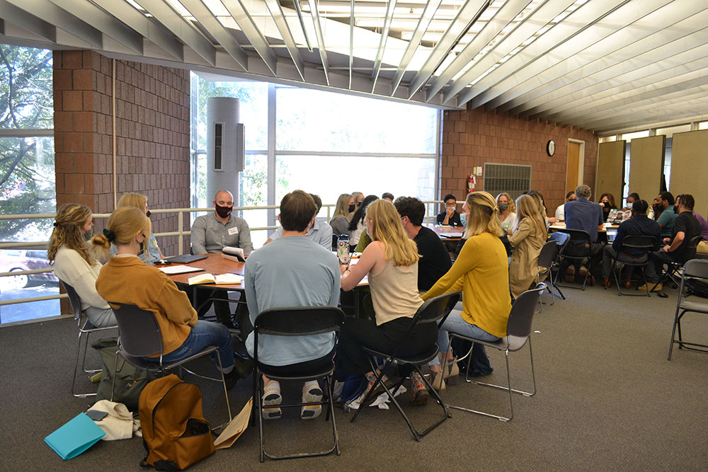 Groups of participants sit around tables in the gallery in Giles.