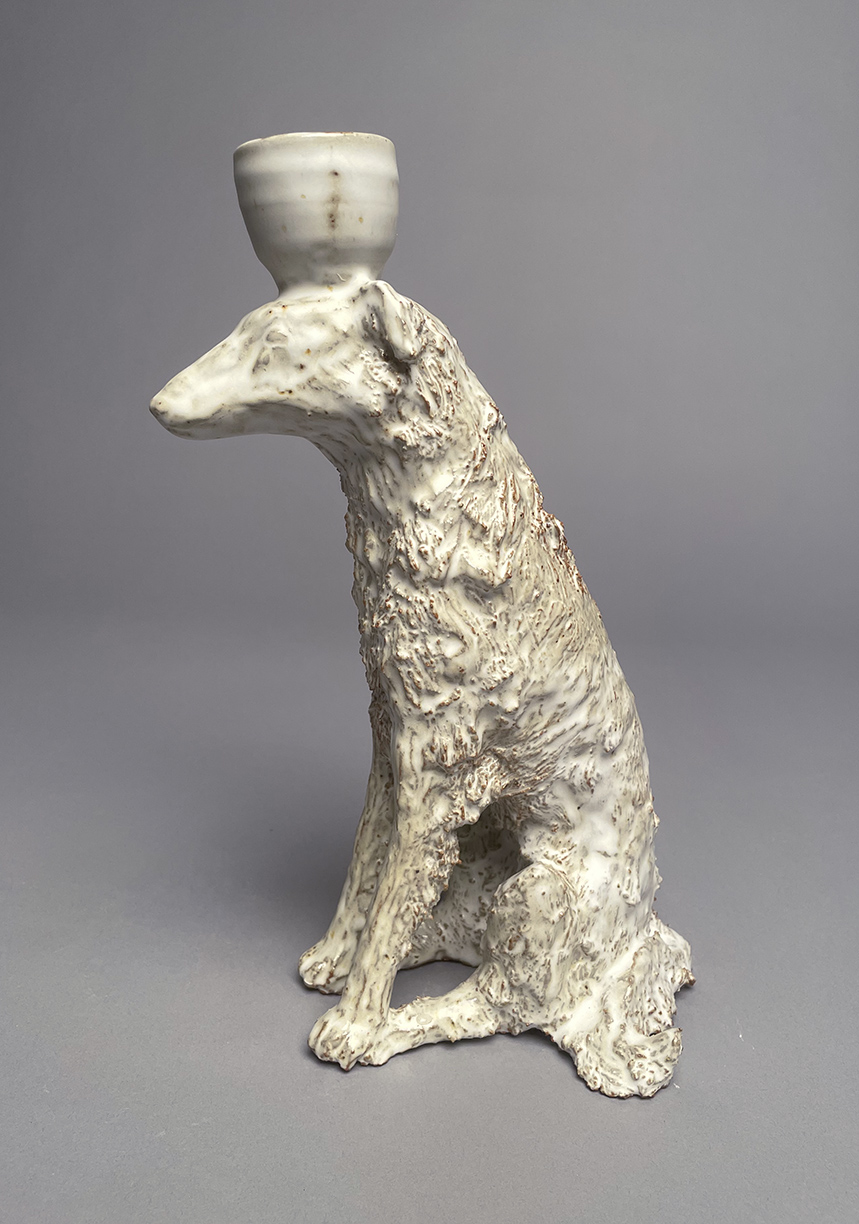 Sculpture of a white dog with a small cup on its head.