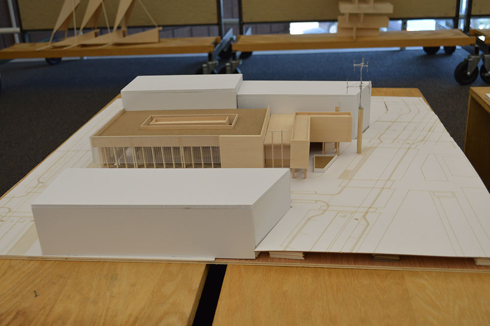 A wooden model of a building that sits on a piece of foamboard for display.
