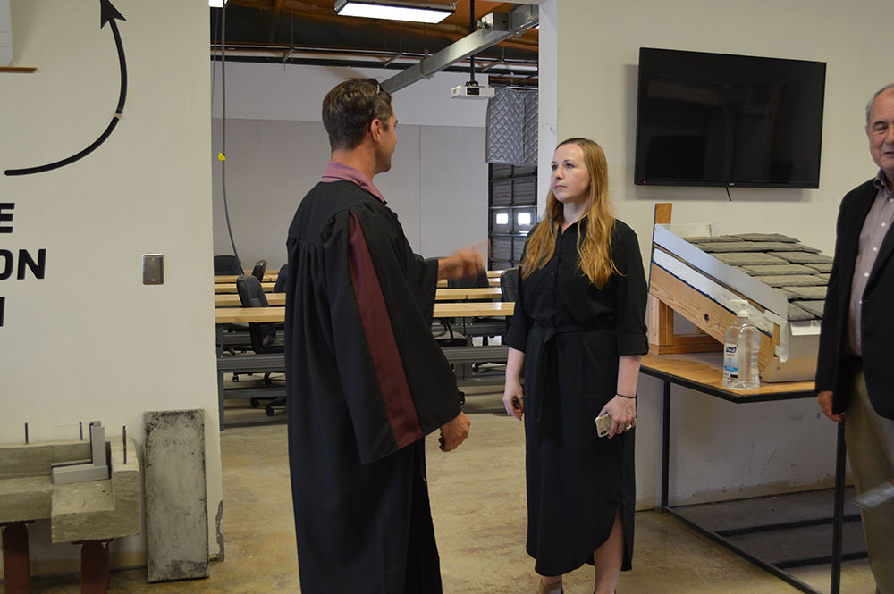 A student dressed in a graduation gown has a conversation with another student.