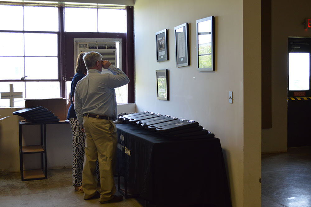 Two people are viewing framed images on the wall.