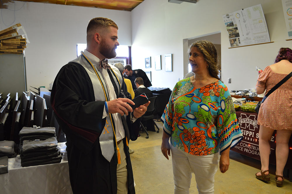 A student in a graduation robe stands and talks with a woman.