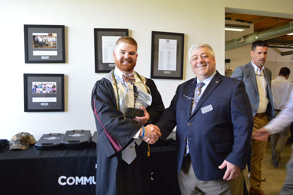 A graduating senior stands with a faculty member shaking hands for a picture.
