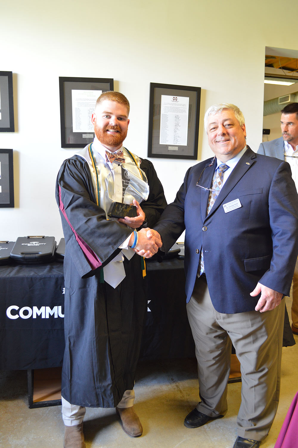 A graduating senior stands with a faculty member shaking hands for a picture.