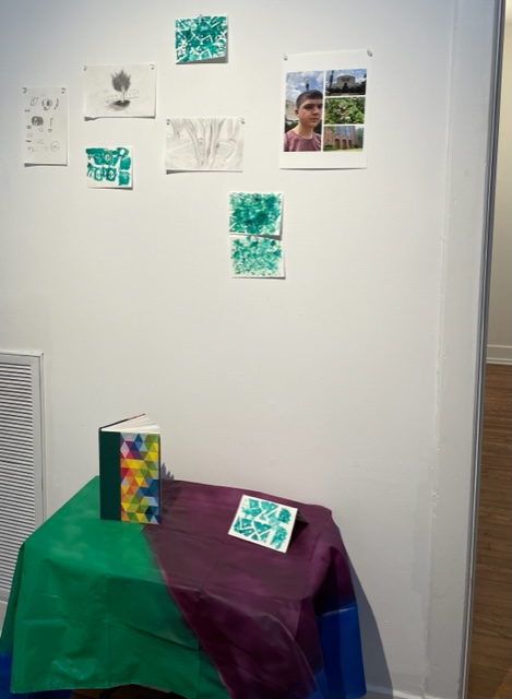 A display of artwork sits on a table and hangs on a wall.