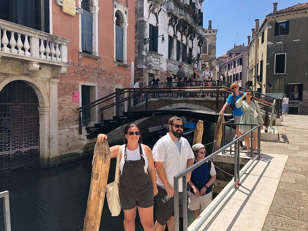 Group stands on structure in canal surrounded by buildings.
