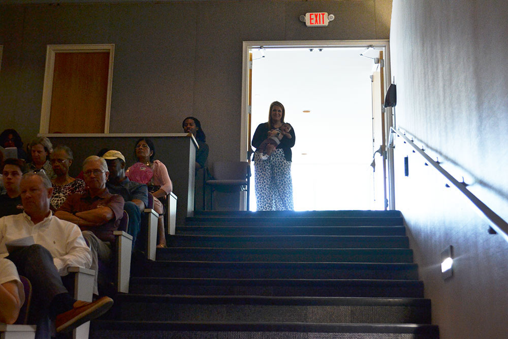 Laura Mitchell stands at top of stairs in the Robert and Freda Harrison auditorium holding a baby