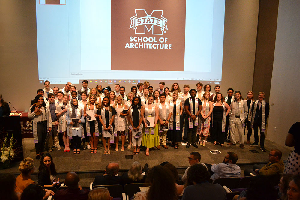 Class of 2023 architecture students pose on stage for a photo in the Robert and Freda Harrison auditorium