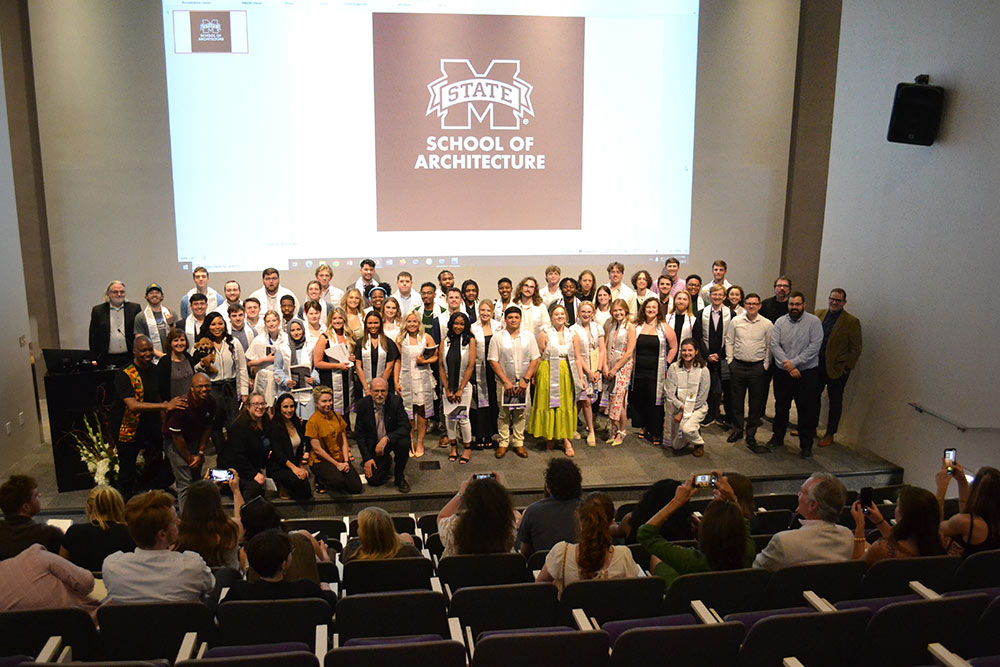 Class of 2023 architecture students and faculty pose on stage for a photo in the Robert and Freda Harrison auditorium