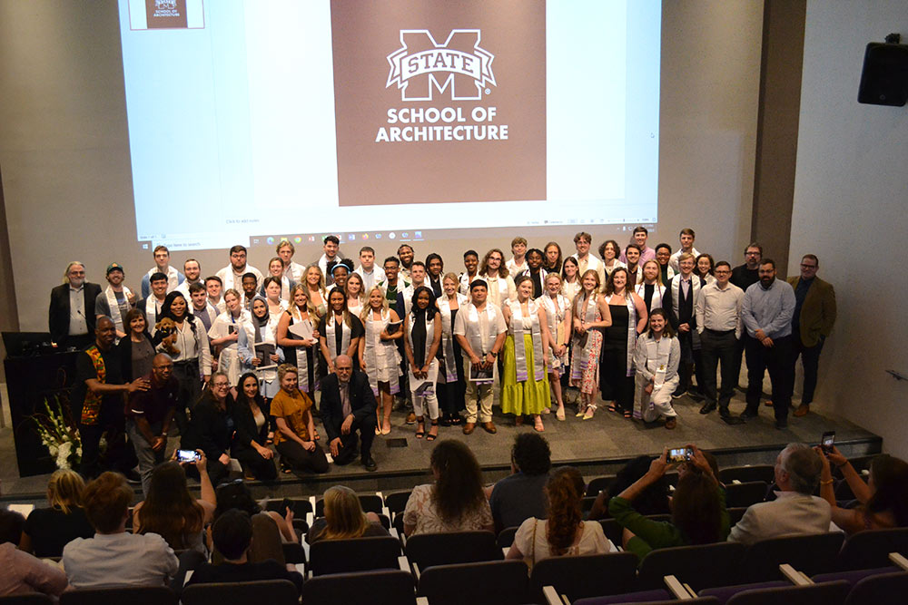 Class of 2023 architecture students and faculty pose on stage for a photo in the Robert and Freda Harrison auditorium