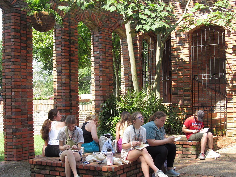 Design Discovery campers sitting outside the Chapel of Memories, sketching in their notebooks.