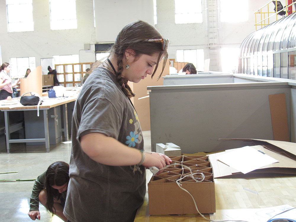 Design Discovery camper works on her cardboard chair project at a desk in Barn.