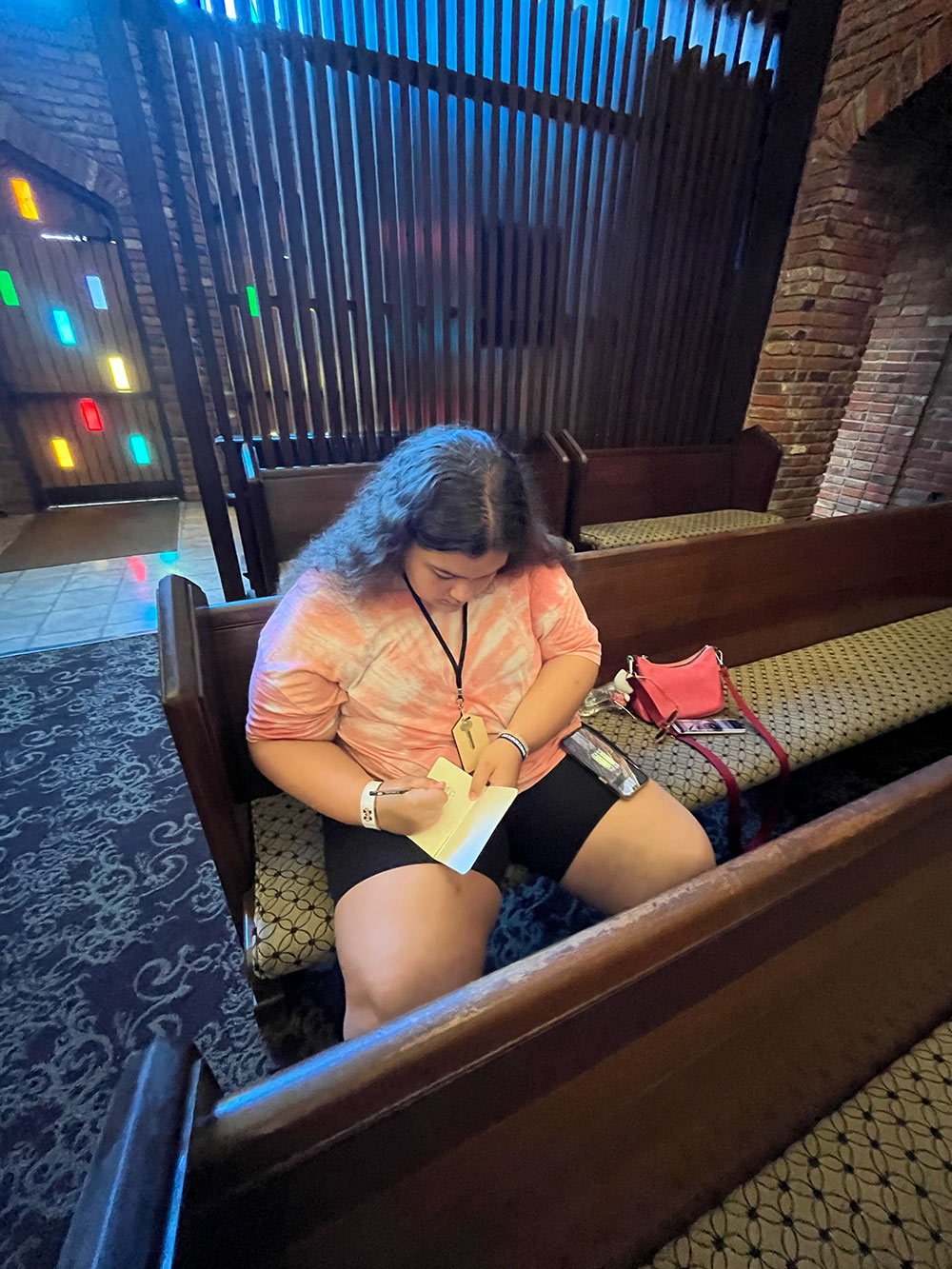 Design Discovery camper sketching in her notebook on a pew in the Chapel of Memories.