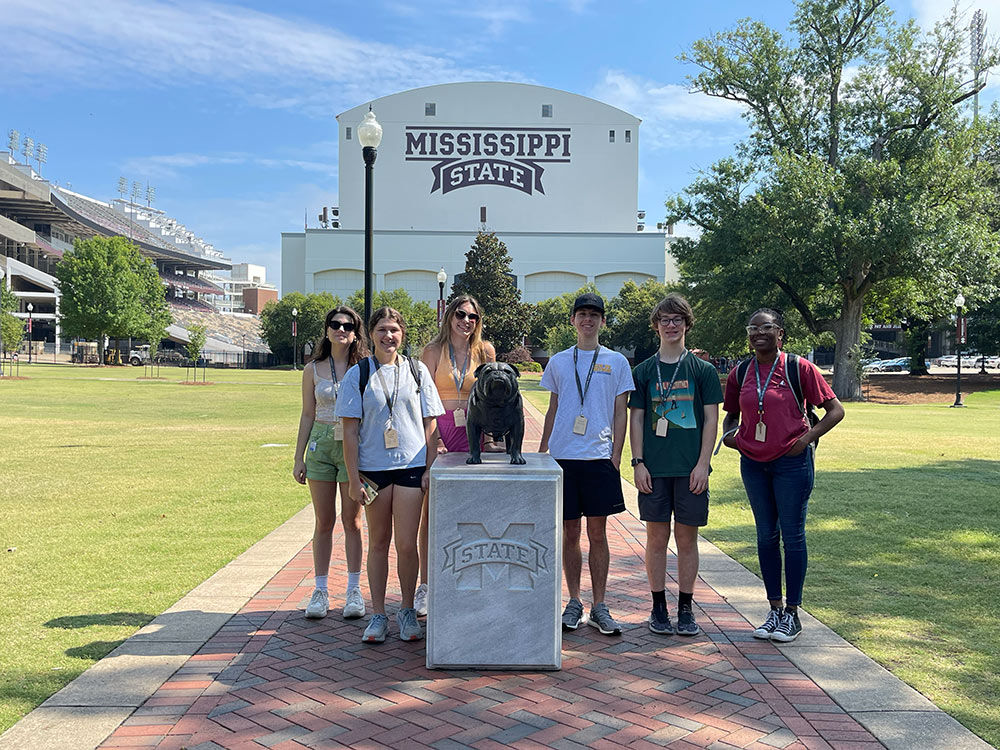 Design Discovery campers pose for a picture by the bulldog statue, in front of the Davis Wade stadium.