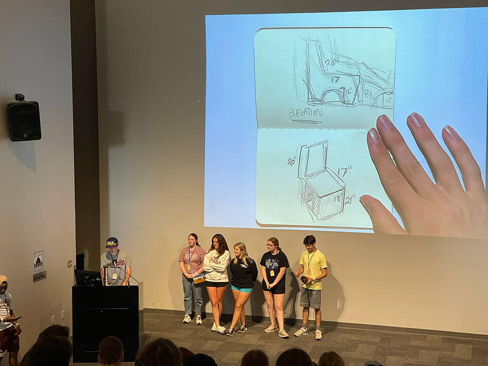 Group of Design Discovery campers presenting their sketches on the projector, to an auditorium full of Design Discovery campers.