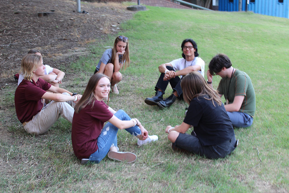 Design Discovery campers and counselors sit outside after finishing their human knot game.