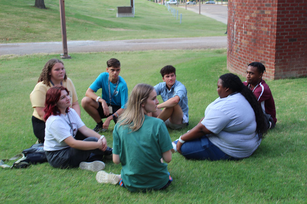 Design Discovery campers and counselors sit outside after finishing their human knot game.
