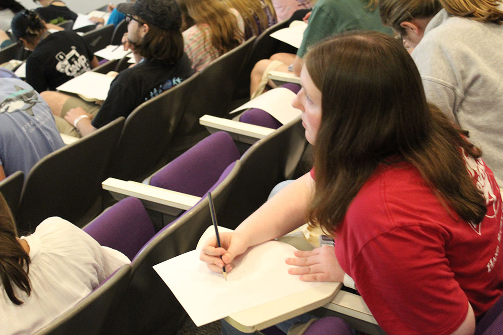 A Design Discovery camper takes notes during a presentation in the auditorium.