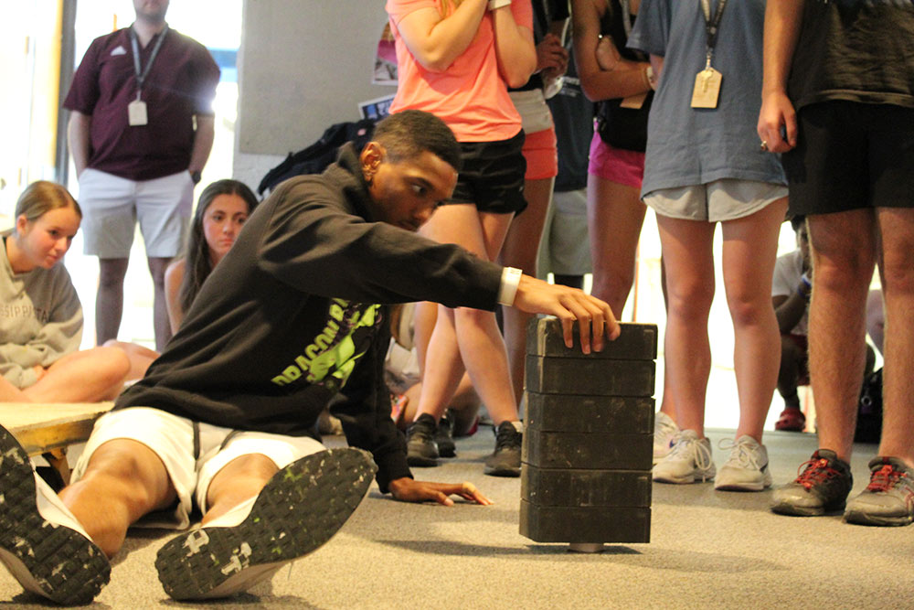 Group of Design Discovery campers observing as one camper places multiple bricks on a small object.