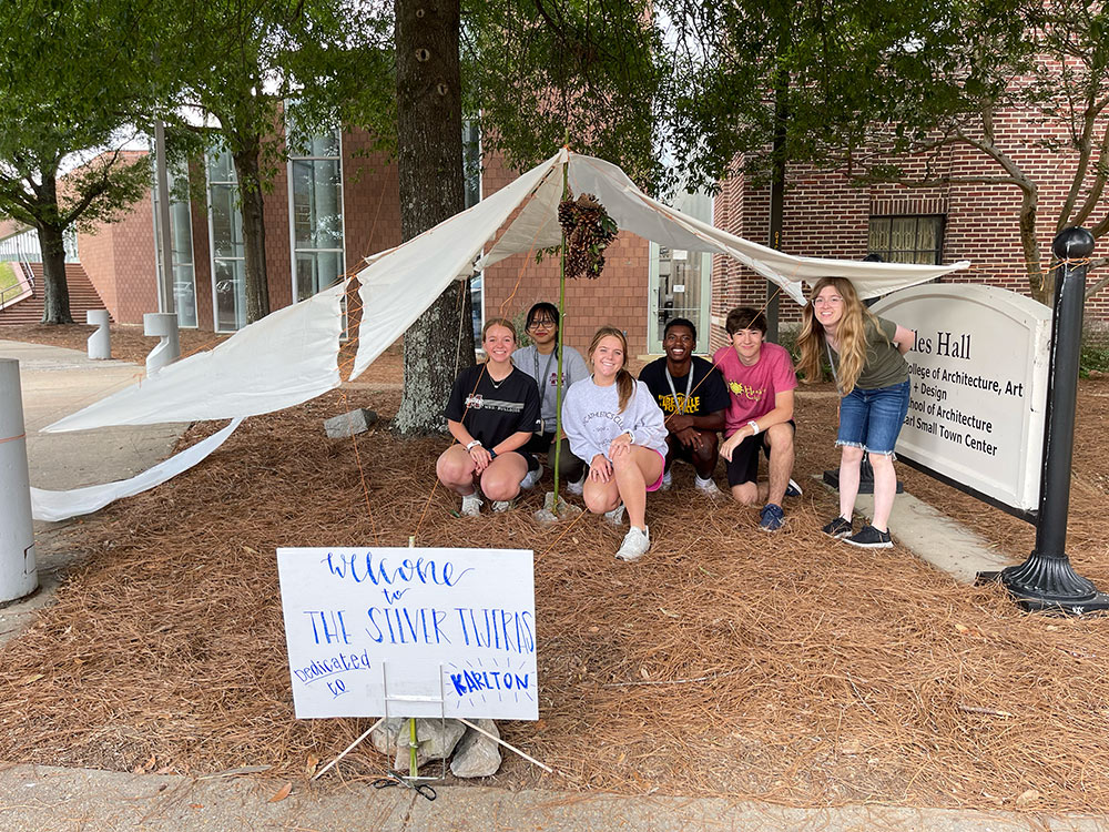 Group of Design Discovery campers posing under their instant environment project, with a sign that reads &quot;Welcome to the Silver Tijeras, dedicated to Karlton.&quot;