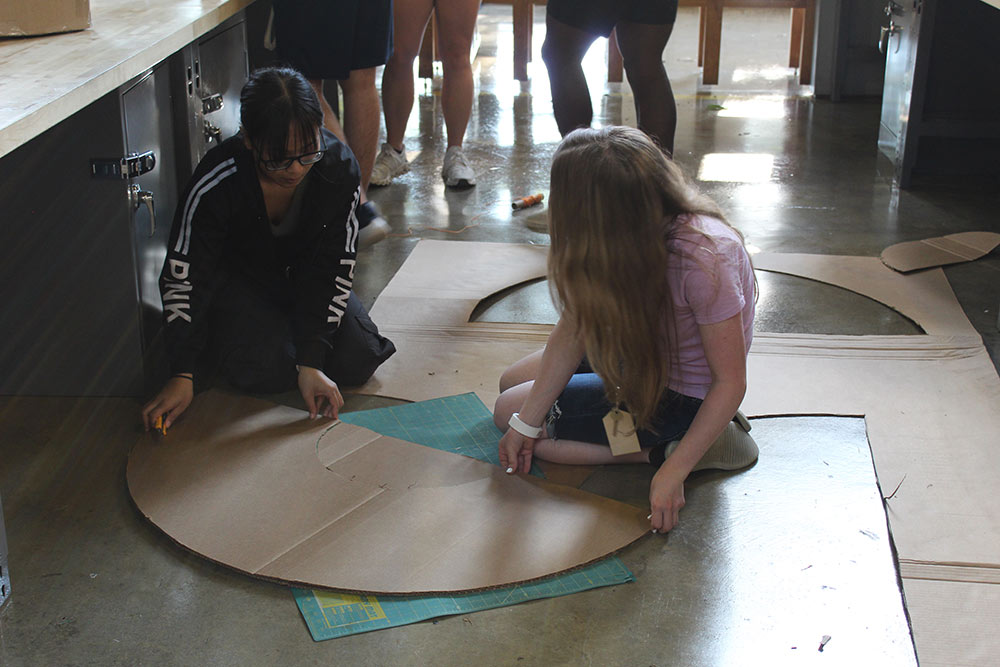 Design Discovery campers work on their cardboard chair project on the floor in Barn.