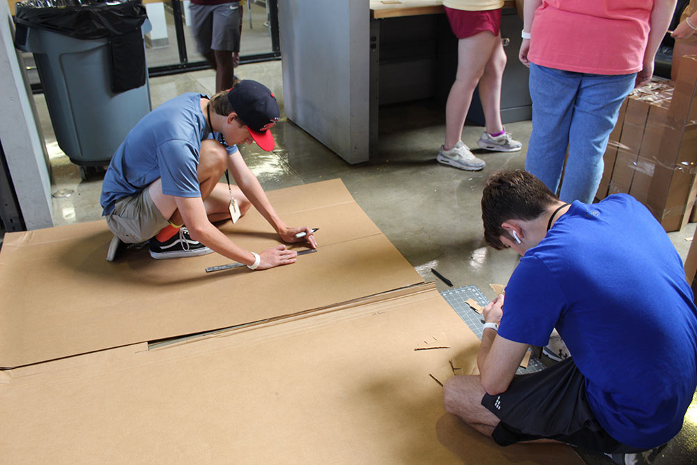 Design Discovery campers work on their cardboard chair project on the floor in Barn.